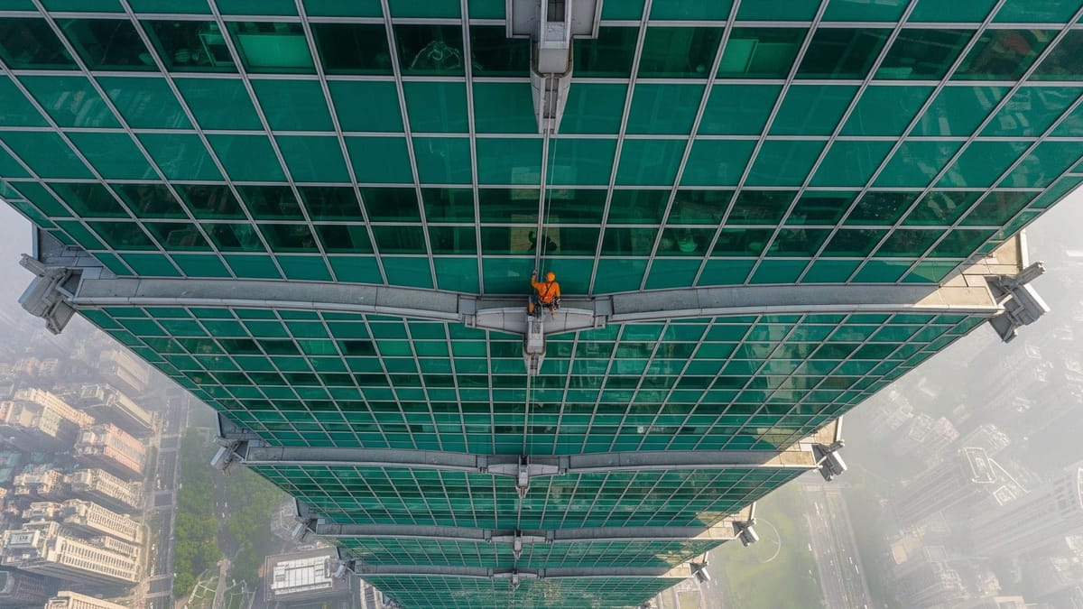 A climber free soloing the exterior glass and steel facade of the Taipei 101 skyscraper, high above the city.