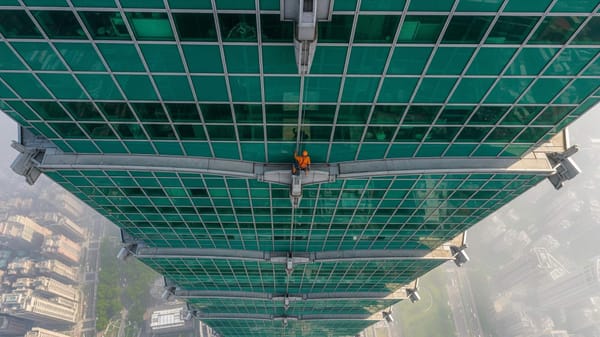 A climber free soloing the exterior glass and steel facade of the Taipei 101 skyscraper, high above the city.